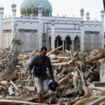 seorang-korban-berjalan-di-antara-batang-batang-pohon-yang-terdampar-di-sebuah-masjid-di-daerah-yang-terdampak-banjir-bandang--1765019325233_169